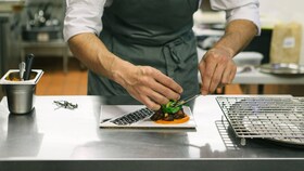 Un chef care așază în farfurie mâncare gourmet prezentată perfect